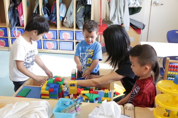 Varios niños meten la mano en una tina de plástico en busca de bloques.