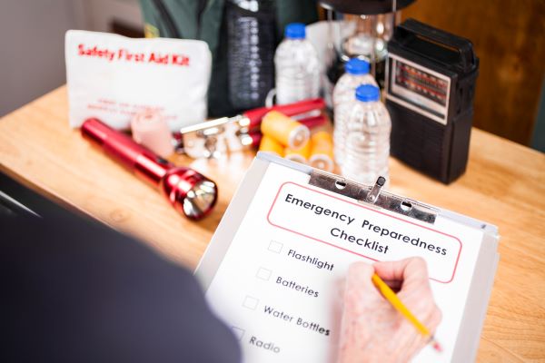 Closeup of a person's hand marking off an emergency preparedness checklist on a clipboard.