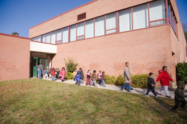 Adults escorting children during an emergency in single file to the outside of a school building.