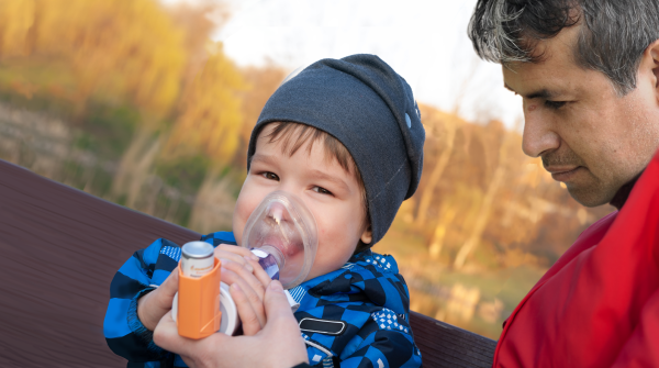 Father helping young boy use an asthma inhaler properly.
